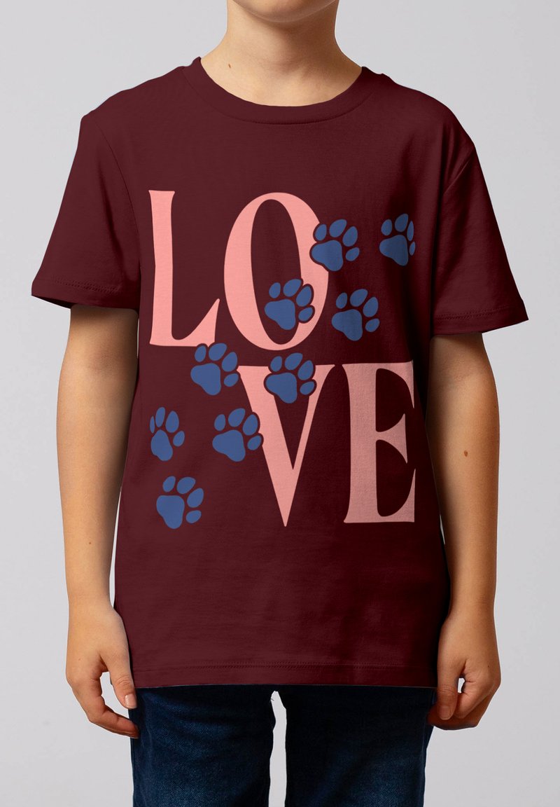 Enfant portant un t-shirt rouge foncé avec de grandes lettres roses formant le mot « LOVE » et des empreintes de pattes bleues dispersées sur le devant.