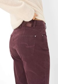 Pantaloni in cotone bordeaux con texture liscia, design a cinque tasche e cuciture rosa a contrasto sulle tasche posteriori. Etichetta con motivo a stelle attaccata.