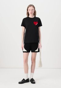 T-shirt en coton noir avec un petit graphique de cœur rouge et le texte "future", associé à un short noir avec des accents blancs incurvés. Mocassins noirs et sac beige.