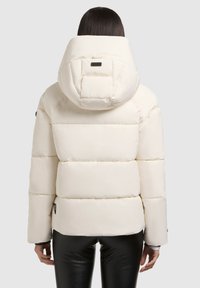 Weißer Pufferjacke mit großer, runder Kapuze, gesteppter Optik und elastischen Bündchen. Getragen mit schwarzen, taillierten Hosen.