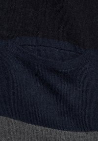 Stickad tröja med en färgblockdesign: mörk marinblå, ljusare marinblå och grå. Mjuk textur med ribbade kanter och en diskret fickdetalj.