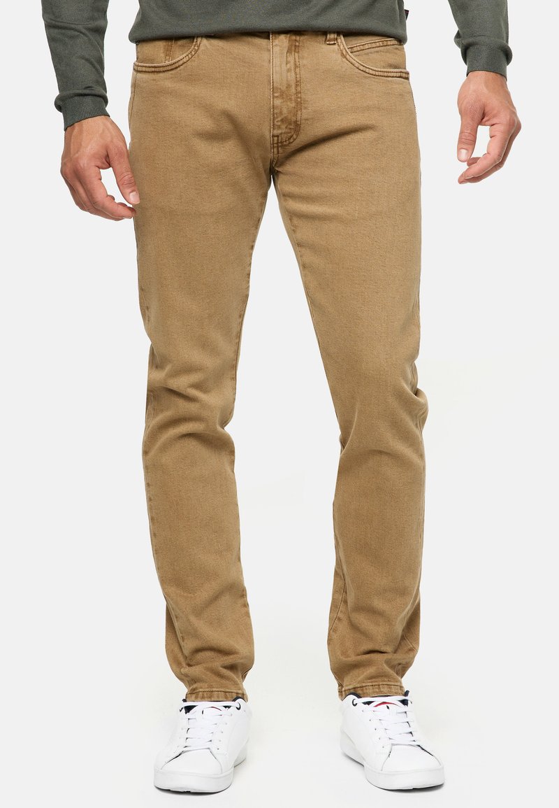 Jeans de algodón color beige con un corte ajustado, que cuentan con cinco bolsillos, detalles de costura sutiles y una textura suave. Combinados con zapatillas blancas.