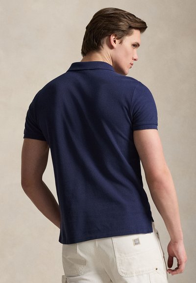 Polo bleu marine en tissu texturé, manches courtes et col classique. Doté d'un ourlet droit et d'un marquage minimal sur le côté.