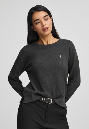 Maglione grigio scuro con scollatura rotonda, maniche lunghe e un piccolo logo bianco sul petto sinistro. Tessuto morbido, vestibilità comoda.