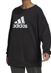 Sudadera negra de mangas largas, de corte oversize, con cuello redondeado y el logo blanco de "adidas" destacado en la parte delantera.