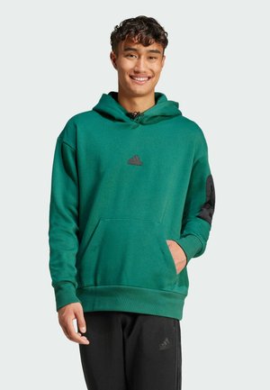Sudadera verde con un bolsillo tipo canguro, logo negro de Adidas en el pecho, cerca de la capucha, con detalles negros en las mangas. Tejido suave y texturizado.