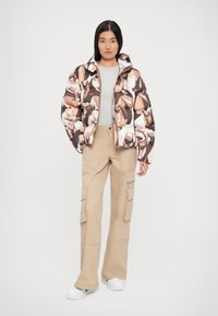 Giubbotto imbottito con una stampa animale geometrica colorata, tonalità marroni e crema. Abbinato a pantaloni cargo beige e sneakers bianche.