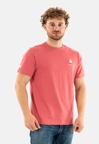 Camiseta de manga corta color coral, hecha de tela suave, con un pequeño gráfico de un velero en el pecho y un logo en la manga.