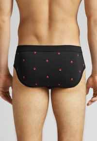 Czarne majtki męskie z wzorem czerwonych biedronek. Materiał wydaje się gładki, z dopasowanym krojem i elastycznym paskiem w talii.