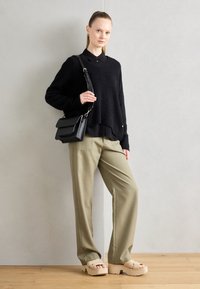 Czarny puszysty sweter na czarnej bluzce z kołnierzykiem, oliwkowe szerokie spodnie i beżowe sandały na platformie, w komplecie z czarną torebką o teksturowej fakturze.