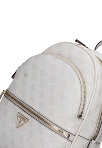Zaino beige chiaro con un motivo a logo, dotato di cerniere in tono dorato, una placca a logo triangolare e tessuto testurizzato.