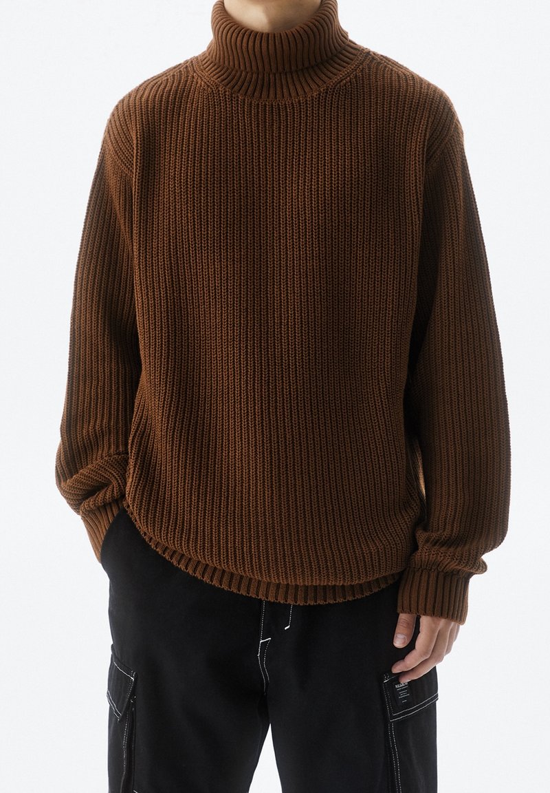 Hnědý žebrovaný rolák z texturovaného pletení. Má volný střih a mírně zakřivený lem, dlouhé rukávy dokončují design.