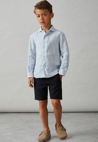Ljusblå linneskjorta med långa ärmar och knäppning fram, ihop med svarta shorts och bruna slip-on skor. Enkelt och avslappnat design.