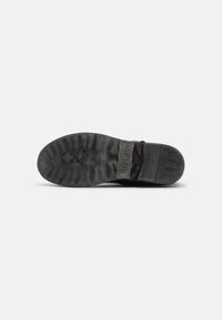 Sola de bota de couro preto com superfície de borracha texturizada, branding em relevo e uma aparência ligeiramente gasta, apresentando um bico arredondado e salto plano.