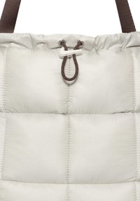 Borsa imbottita grigia chiara con texture trapuntata, dotata di un cordoncino marrone e occhielli argentati. Tessuto resistente e spallacci marroni regolabili.