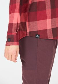 Rød og lyserød rutet flannel skjorte med knapmanchetter, parret med mørkeburgunder bukser, med et distinkt logo-tag ved kanten.