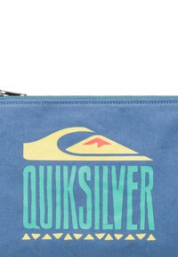 Blå tygpåse med en gul och röd våglogotyp och fet "QUIKSILVER"-text i grönt, med ett geometriskt mönster i gult längst ner.