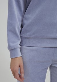 Fleece-Pullover und Hose in hellem Lavendel. Gerippte Textur, lange Ärmel und entspannte Passform. Die Bündchen sind für mehr Komfort elastisch.