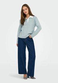 Blusa de manga larga a rayas en azul claro con un cuello blanco, combinada con unos jeans de pierna ancha en azul oscuro y sandalias de tacón azules.