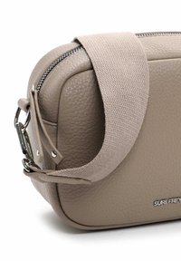 Beige Lederhandtasche mit strukturierter Oberfläche, ausgestattet mit einem Stoff-Schulterriemen, silbernen Beschlägen und einem Reißverschluss. Logo auf der Vorderseite geprägt.