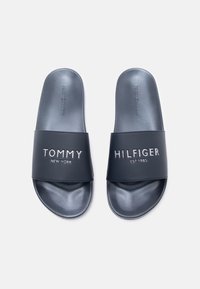 Sandalias tipo slide azul marino hechas de material sintético. Cuentan con una correa ancha con branding en relieve: "TOMMY NEW YORK" y "HILFIGER EST.1985."