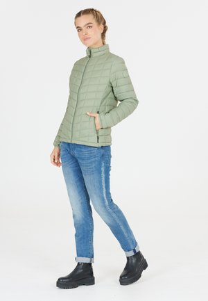 Veste matelassée verte avec col montant, fermeture éclair et poches latérales, associée à un jean bleu et des bottines noires. Texture lisse et design léger.