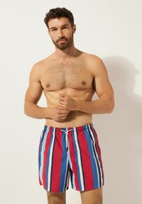 Bañador a rayas con líneas verticales rojas, azules y blancas, con cintura elástica y cordón para un ajuste ajustable.