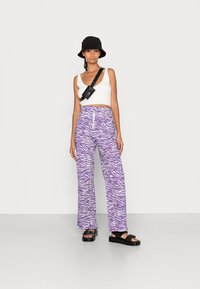 Calças largas com padrão de zebra em roxo e branco, usadas com um top curto felpudo branco e um chapéu preto tipo balde. Sandálias de plataforma pretas e uma bolsa crossbody.