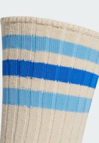 Béžová ribbovaná bavlněná ponožka s horizontálními pruhy v různých odstínech světlé a tmavé modré. Texturovaný povrch.
