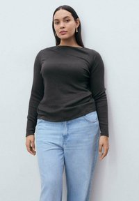Bluză cu mânecă lungă, de culoare gri închis, dintr-un material moale, asortată cu jeansi drepți de culoare bleu deschis, având un design simplu, mulat.