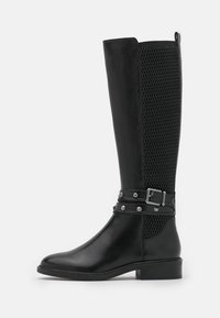 Bottes noires montant jusqu'au genou avec un avant en cuir lisse et un panneau en maille texturée. Ornées d'une sangle cloutée et de ferrures argentées.
