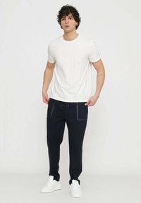 T-shirt en coton blanc à col rond, associé à un pantalon de jogging bleu marine avec deux poches latérales et des finitions grises, complété par des baskets blanches.