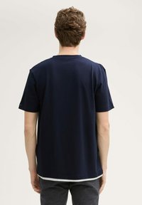 T-shirt blu navy con motivo testurizzato, colletto a giro, maniche corte e vestibilità comoda. Il tessuto sembra leggero e traspirante.