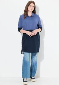 Sininen ja tummansininen väri-lohkottu tunika, jossa on pitkät hihat ja kaulus, sivuilla rypytystä ja yhdistetty kevyesti flare-mallisille denim-farkuille.