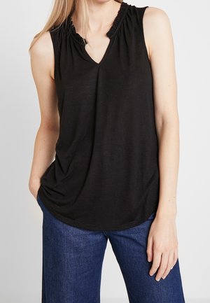 Zwart mouwloos topje met een V-hals en ruches langs de halslijn, gemaakt van zachte stof, gecombineerd met wijde blauwe spijkerbroek.