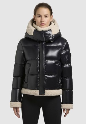 Svart vadderad jacka med en blank yta, med en beige fleece-fodrad huva och nederkant. Designen inkluderar en framzip och sidfickor.