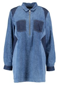 Camicia di denim in diverse tonalità di blu, con chiusura a mezza zip frontale, colletto e due tasche sul petto. Maniche lunghe con dettagli a contrasto.