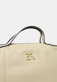 Borsa a mano in pelle crema con rifiniture nere e logo dorato in rilievo con le lettere "F" e "R" sulla parte anteriore.