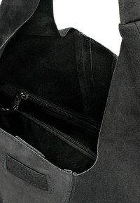 Borsa in suede nero con apertura ampia sulla parte superiore, dotata di una tasca interna con zip e foderata in tessuto liscio. Include un'etichetta di branding discreta.