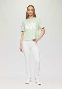 Hellgrünes, kürzes T-Shirt mit dem Aufdruck "love" in Weiß, kombiniert mit weißen Slim-Fit-Hosen und beigen Sneakern. Einfaches Design und lockere Passform.