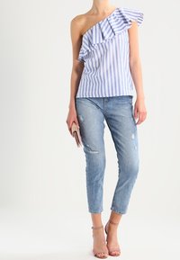 Top azzurro chiaro e bianco a righe con spallina unica e rifiniture arricciate, abbinato a jeans corto strappati azzurro chiaro e sandali beige con listini.