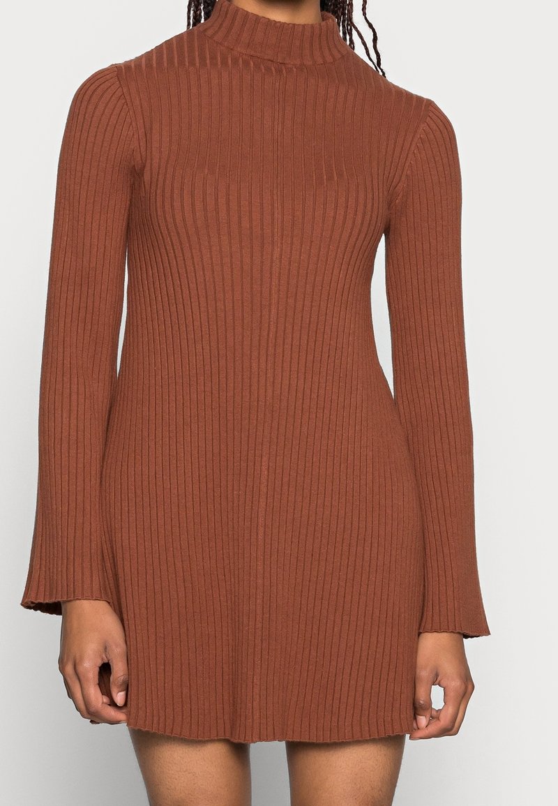 Robe marron côtelée avec un col haut et des manches longues, présentant une silhouette ajustée et des extrémités de manches évasées. Texture de tissu douce.