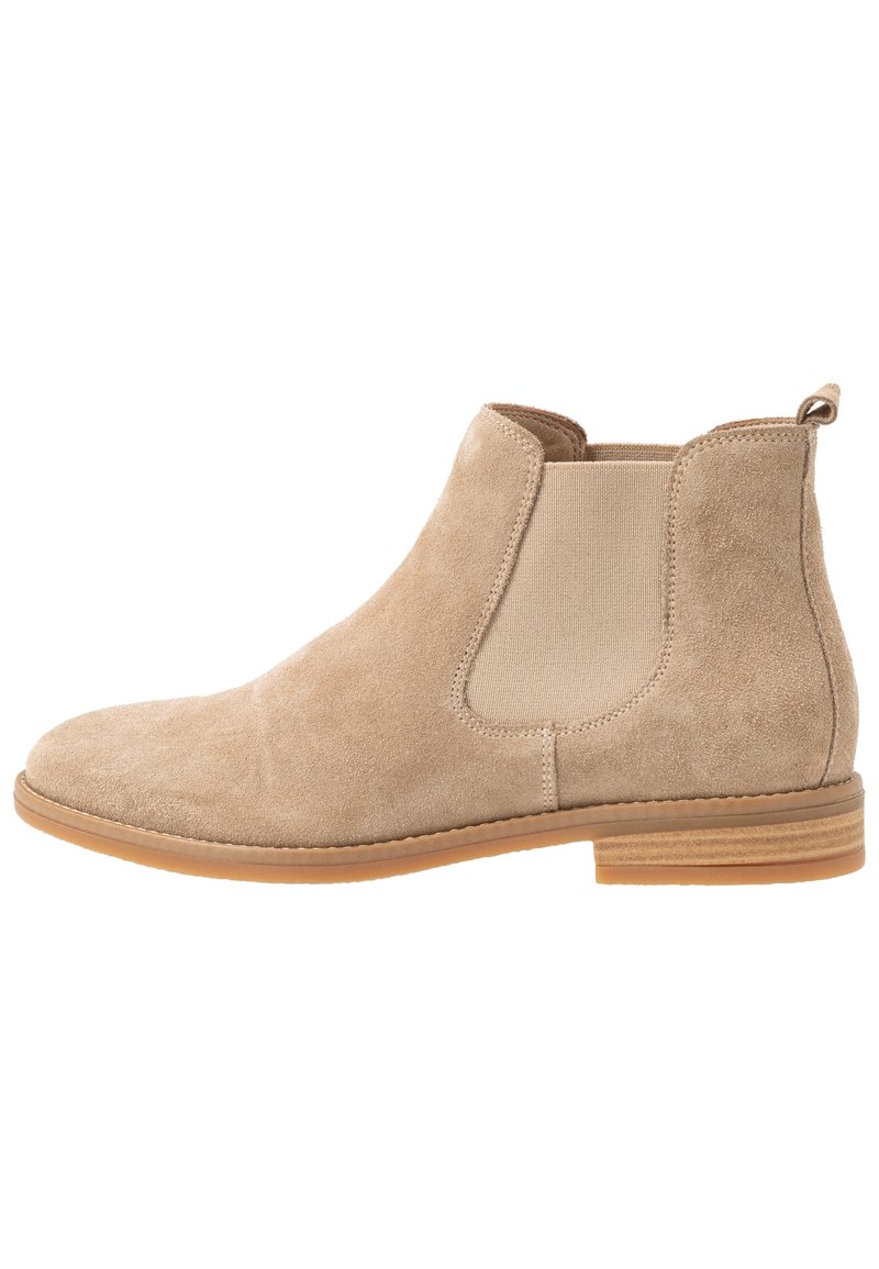 Bottine Chelsea en daim beige avec panneau latéral élastique, languette à l'arrière et semelle basse en bois empilée.