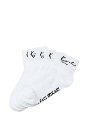 White cotton socks featuring a black logo and design on the ankle. The socks have a ribbed texture and a crew length style.