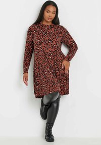 Långärmad leopardmönstrad klänning i rost och svart, med rund halsringning och avslappnad passform, i kombination med svarta leggings och snörstövlar.