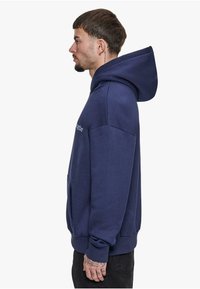 Granatowy hoodie wykonany z mieszanki bawełny, z przestronnym kapturem, kieszenią z przodu i ściągaczami przy mankietach. Minimalistyczny design z subtelnym logo.