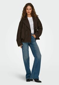Bruine dubbel-breasted blazer met brede revers, gecombineerd met lichtblauwe distressed flared jeans en zwarte enkelboots.