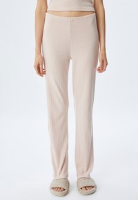 Lichtroze pyjamabroek met een geribbelde textuur en kleine verhoogde patronen, voorzien van een tailleband met aantrekkoord en een losse pasvorm, gecombineerd met fuzzy pantoffels.