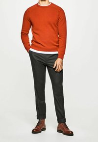 Punainen neulottu villapaita, jossa on resorireunainen pääntie, yhdistetty tummanharmaisiin räätälöityihin housuihin ja ruskeisiin nahkaisiin nauhakenkiin. Tyylikäs ja vartalonmyötäinen malli.