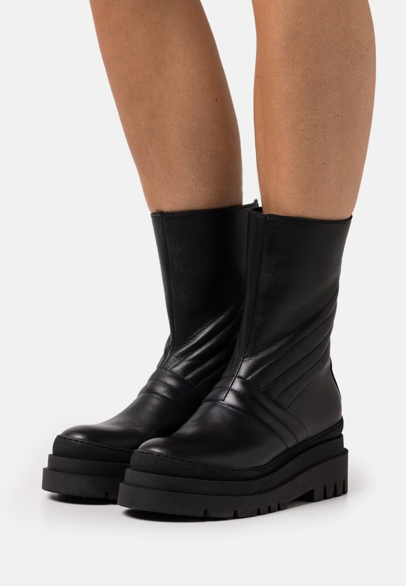 Černé kožené kotníkové boty s vertikálním žebrovaným designem, silnou černou podrážkou a zaoblenou špičkou. Zapínání na zip na vnitřní straně boty.